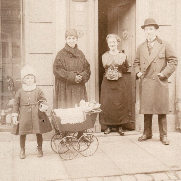 People In Stylish Clothes With Hats And Coats In Front Of A Building Door And A Cute Girl With A Doll Pram