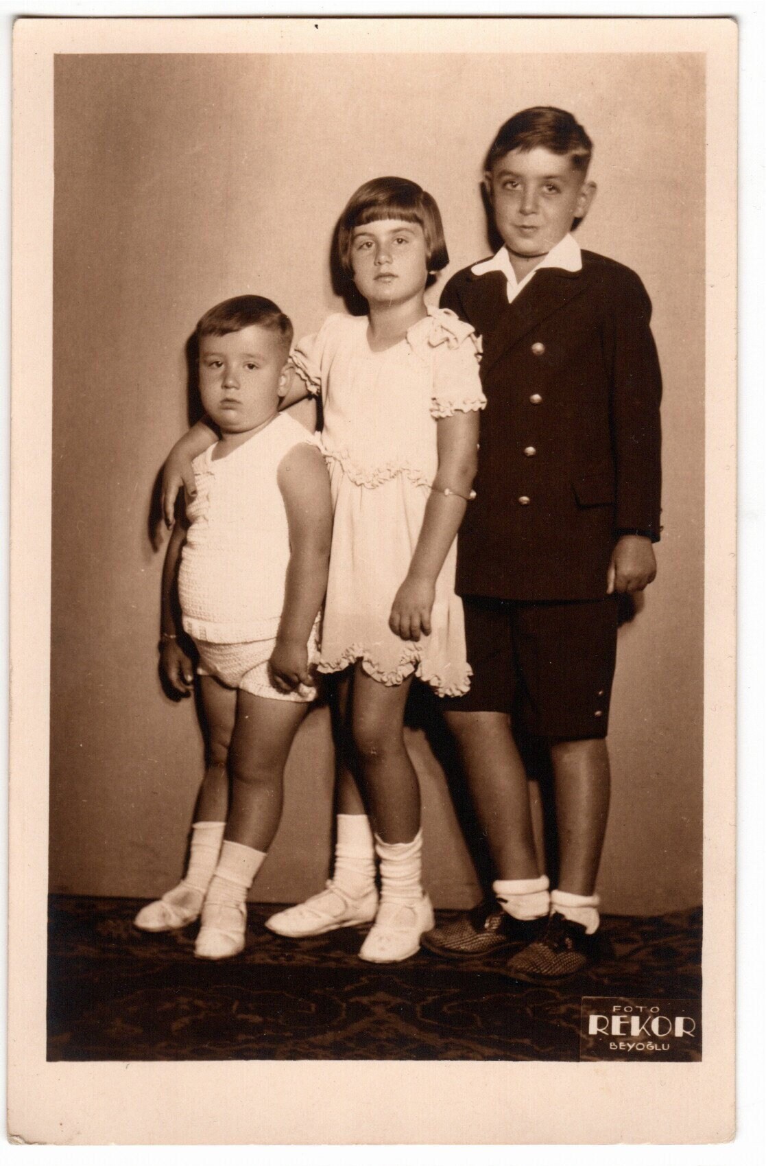 Fotografía sepia de tres niños con estilo, ordenados por estatura