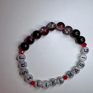 Könnte beinhalten: Ein Armband aus Perlen mit den Worten "JUST LIKE MAGIC" in schwarzen Buchstaben auf transparenten Perlen. Das Armband hat abwechselnd schwarze, rote und transparente Perlen. Rote Kristallperlen sind im Design verstreut.
