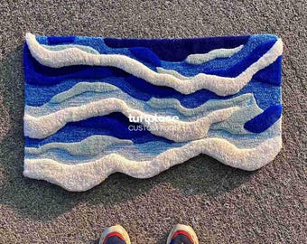 May include: A rectangular custom rug with a wavy design in shades of blue and white. The rug features the text "tuftplace CUSTOM RUGS". The rug is placed on a textured surface. The rug's design resembles ocean waves.
