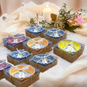 Può includere: Una collezione di piccole ciotole rotonde in ceramica in vari colori, tra cui giallo, arancione e blu, ognuna caratterizzata da intricati motivi floreali. Ogni ciotola è confezionata in una scatola di plastica trasparente con base marrone, legata con spago.