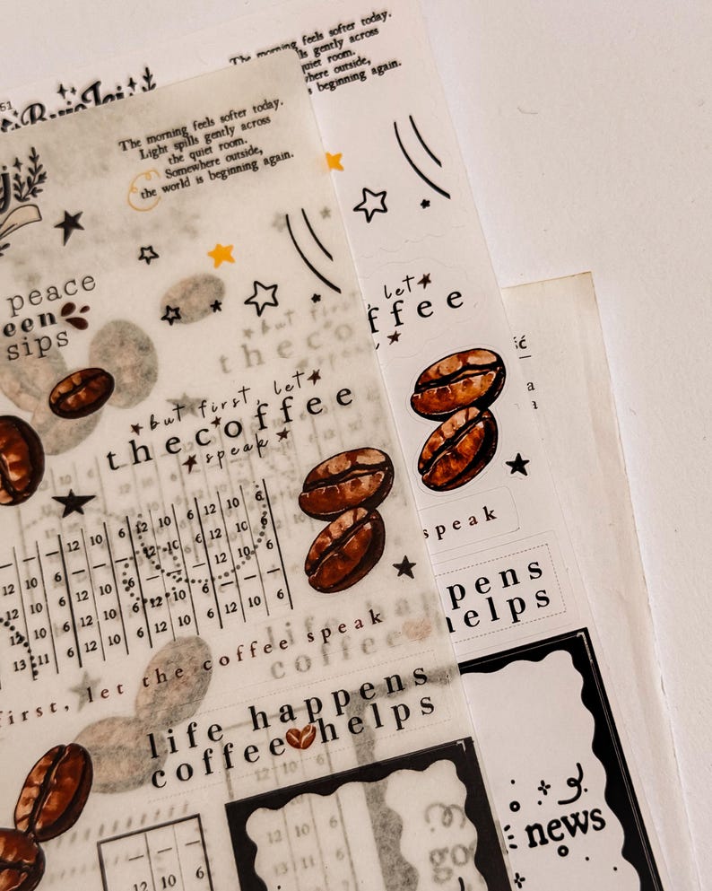 May include: Overhead shot of coffee-themed decorative stickers. The stickers feature coffee beans, stars, and text like "the coffee" and "life happens coffee helps." The stickers are on a translucent background.