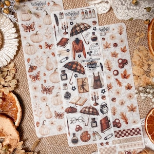 May include: Three decorative sticker sheets with fall-themed illustrations. The stickers feature pumpkins, butterflies, leaves, umbrellas, and clothing. The text "Stressed Blessed Obsessed" is visible on one sheet. The color palette includes shades of brown, beige, and orange.