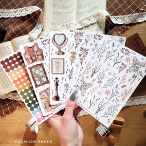 May include: Four sheets of floral themed stickers with a variety of designs. The stickers feature flowers, leaves, crosses, and other botanical elements. The stickers are printed on white paper and have a matte finish.