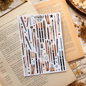 Op de afbeelding: Een rechthoekig stickervel met diverse illustraties van pennen, potloden, penselen en kleine kantoorbenodigdheden zoals een paperclip en gum, afgewisseld met kleine ster- en hartjesiconen, met de tekst BujoJej bovenaan.
