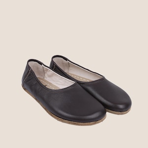 May include: A pair of dark brown leather ballet flats. The shoes have a rounded toe, a low profile, and a stitched sole. The interior is a light color, and the shoes appear to be unworn. The background is a solid, neutral color.