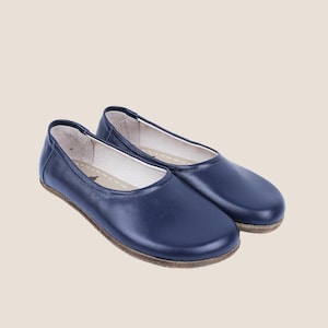 May include: A pair of navy blue leather ballet flats. The shoes have a rounded toe and a low profile, with a stitched sole and a white interior. The shoes are designed for comfort and style.