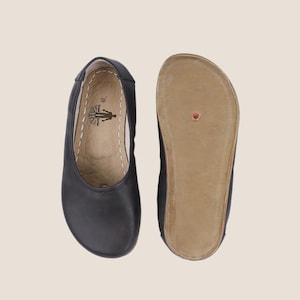 May include: Black leather ballet flats, one showing the sole. The sole is a light brown color. The interior of the shoe has a logo and the number 39. The shoes are designed with a rounded toe and a low profile.