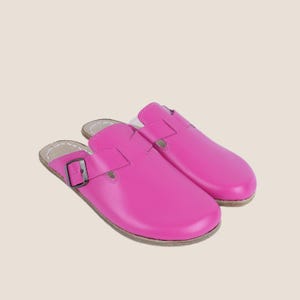 May include: A pair of bright pink leather clogs. The clogs have a buckle closure and a rounded toe. The soles are a light brown color. The clogs are designed for comfort and style.