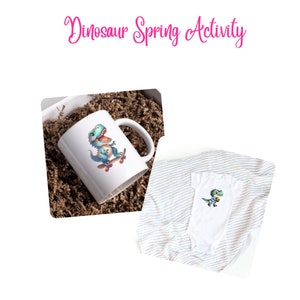May include: A white mug with a cartoon dinosaur on a skateboard. The dinosaur is green and blue and has a toothy grin. The mug is sitting in a brown paper gift bag. A white onesie with a similar dinosaur design is also shown.