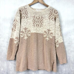 May include: A beige and white knitted sweater with a snowflake pattern. The sweater has long sleeves and a round neckline.