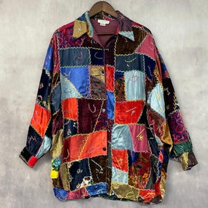 May include: A long-sleeve button-down shirt featuring a patchwork design of various velvet and satin fabric squares in shades of red, blue, purple, and gold. The panels are joined by visible yellow decorative stitching and a collar.