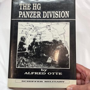 May include: A hardcover book titled The HG Panzer Division by Alfred Otte, published by Schiffer Military. The black and white cover features a historical photograph of soldiers with a military vehicle and a detailed tactical map of the region.