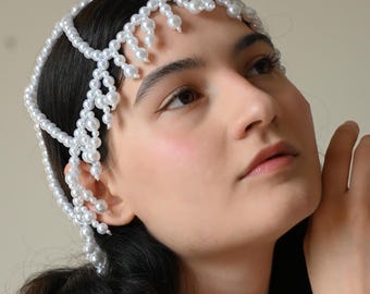 May include: A white pearl headband with a cascading fringe of pearls. The headband is worn by a person with dark hair.