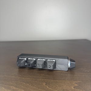 May include: A black, rectangular device with four raised, square buttons, each labeled with a number. The device is resting on a wooden surface. The buttons are labeled with the numbers 1, 4, 2, and 2.