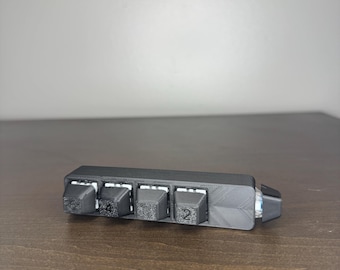May include: A black, rectangular device with four raised, square buttons, each labeled with a number. The device is resting on a wooden surface. The buttons are labeled with the numbers 1, 4, 2, and 2.