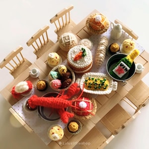 May include: A miniature crocheted picnic scene with a variety of food items, including a red lobster, cake, bread, and a bottle of wine. The scene is set on a wooden table with miniature chairs.