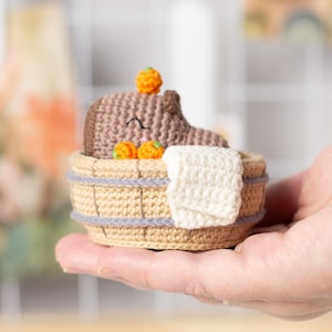 May include: A crocheted brown animal with orange accents is relaxing in a crocheted beige bathtub with a white towel.