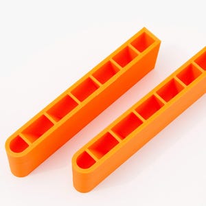 Op de afbeelding: Twee feloranje, rechthoekige organizers met meerdere compartimenten. Elke organizer heeft een afgerond uiteinde en een reeks gelijkmatig verdeelde, vierkante openingen. De items staan tegen een witte achtergrond.