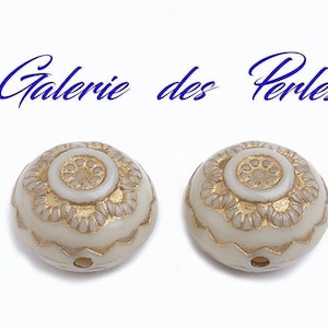 Puede incluir: Dos cuentas redondas blancas con detalles dorados y un agujero en el centro. Las cuentas tienen un diseño decorativo con un círculo central elevado y un borde festoneado.