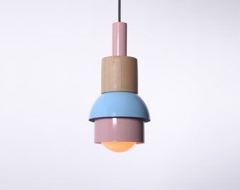 Può includere: Una lampada a sospensione con una base in legno e tre paralumi. Il paralume superiore è rosa, il paralume intermedio è azzurro chiaro e il paralume inferiore è rosa.