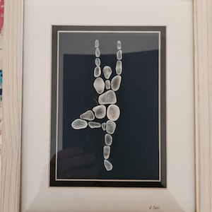 Könnte beinhalten: Gerahmtes Kunstwerk mit einer Tänzerin aus Meeresglas. Die Tänzerin ist in einer Ballettpose vor einem dunkelblauen Hintergrund dargestellt. Der Rahmen ist aus hellem Holz. Das Kunstwerk ist unten rechts signiert.