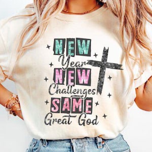 May include: A white t-shirt with a graphic design that says "New Year New Challenges Same Great God" with a glittery cross.