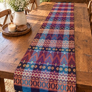 Puede incluir: Un camino de mesa rectangular largo con un patrón tejido vibrante que presenta bandas horizontales de formas geométricas, zigzags y diamantes en tonos morado intenso, azul brillante, naranja y amarillo, acabado con borlas.