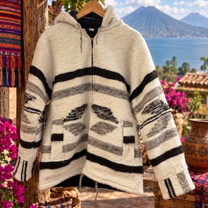 May include: A zip-up hooded jacket in an off-white, gray, and black color palette. The garment features a textured weave with horizontal stripes and geometric patterns across the chest and sleeves, two front pockets, and a black interior lining.