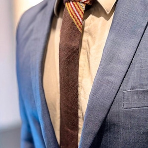 May include: A close-up of a blue suit jacket with a brown tie. The tie has a textured appearance with red, yellow, and white stripes. The shirt underneath is a light tan color.