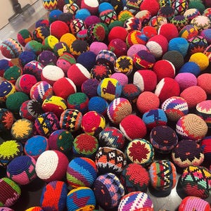 May include: A collection of colorful, hand-crocheted hacky sacks. The balls feature a variety of colors and patterns, including red, white, blue, yellow, and green. The hacky sacks are made of yarn and are designed for footbag play.