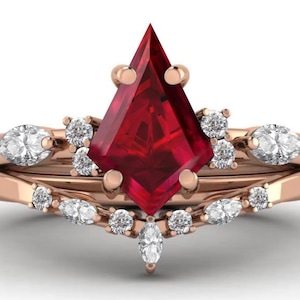 May include: A rose gold ring set featuring a kite-shaped, deep red gemstone as the centerpiece. The ring is accented with multiple small, round, and marquise-cut white gemstones. The set includes a curved band.