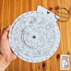 May include: A white paper wheel calendar with a rotating inner dial, featuring months, days, and weather-related illustrations. The calendar is held by a hand and includes the text "digitaler Download".