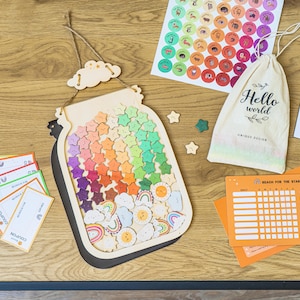 May include: Wooden jar-shaped reward chart filled with colorful star-shaped tokens. Includes a drawstring bag with "Hello World" text, sticker sheets, and reward cards. The chart is designed to track progress and encourage positive behavior.