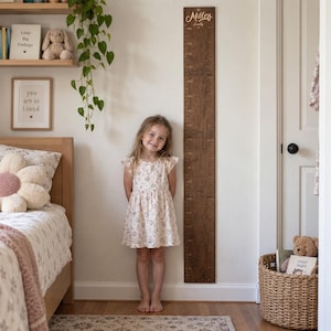 May include: A tall, rectangular dark brown wooden growth chart mounted on a wall, featuring engraved measurement markings and the text The Millers Family at the top. The board has a visible wood grain texture and a vertical scale.
