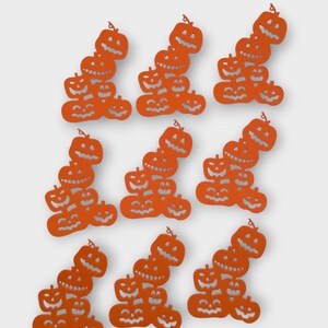 May include: A set of nine orange die-cut decorations, each featuring a vertical stack of four carved jack-o'-lantern pumpkins with distinct facial expressions, including triangular eyes and jagged mouths, arranged in three rows of three individual pieces.