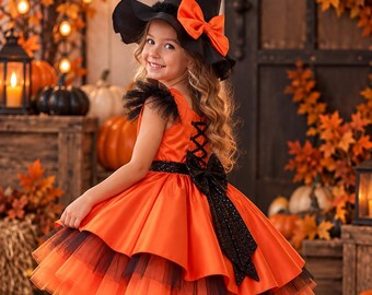 Puede incluir: Un vestido naranja brillante con falda de tul en capas, detalles de volantes negros en los hombros y una espalda con cordones negros y un lazo grande. El conjunto incluye un sombrero de bruja negro puntiagudo con un lazo naranja y zapatos de charol.