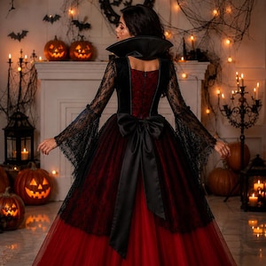 May include: A floor-length gown featuring a deep red velvet bodice with a high black collar and long black lace sleeves. The skirt consists of layered red tulle with a black lace overlay, accented by a large black satin bow at the waist.