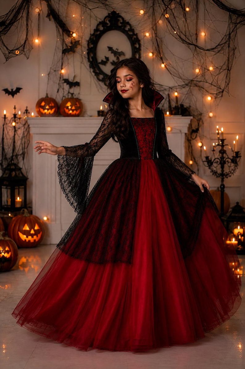May include: A floor-length gown featuring a deep red velvet bodice with a square neckline and a high, stiffened collar. The long, flared sleeves are made of black lace, matching the black lace overlay that drapes over the full, layered red tulle skirt.