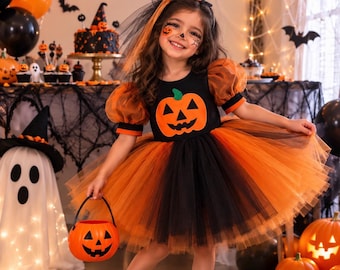 May include: A black and orange Halloween dress featuring a pumpkin applique on the bodice, sheer puff sleeves, and a layered tulle skirt. The outfit includes a matching mini cone hat with a black veil and a small orange plastic pumpkin bucket.