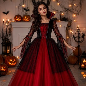 May include: A floor-length gown featuring a deep red bodice with a black velvet overlay, a high standing collar, and long flared sleeves made of black lace. The skirt consists of a voluminous red tulle base layered with black lace panels.