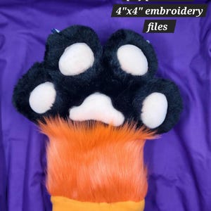 Könnte beinhalten: Eine Plüschpfote mit schwarzem Fell und weißen Ballen, die in orangefarbenes Fell und eine gelbe Manschette übergeht. Der Text "pdf pattern+ 4"x4" embroidery files" ist sichtbar.