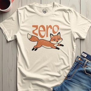 May include: Cream-colored t-shirt featuring a cartoon fox in orange and white, with the word "zero" in orange above it. The fox is running with a smile. The shirt has a Fifth Kitty logo on the neckline.