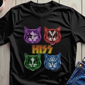 Pode incluir: Camiseta preta com quatro rostos de gato no estilo da banda de rock KISS. Os gatos são roxos, vermelhos, verdes e azuis, cada um com designs de maquiagem exclusivos. A palavra "HISS" é impressa em dourado abaixo.