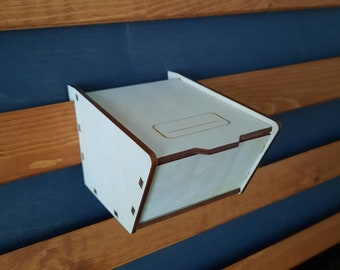 May include: A white wooden wall mounted box with a small opening on the top. The box is angled slightly forward.