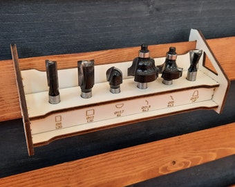 May include: A white wooden rack with eight slots for holding router bits. The rack has labels for each slot, including "Ø12 L20", "Ø12.7 R6", "Ø21.8 R6.3", "Ø25 R4.5", and "Ø12.7 1/4".