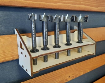 May include: A white wooden tool holder with six slots for holding drill bits. The holder is mounted on a wooden wall. The drill bits are black and have the Bosch brand name printed on them.