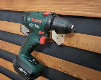 May include: A green and black cordless drill with a white plastic holder attached to a wooden wall. The drill has the Bosch logo and the text "14.4V Li-Ion" on it.
