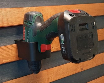 May include: A black wall mount holder for a green and black cordless drill. The drill has a black battery pack with the text "14.4 V 1.5 Ah" printed on it. The drill also has the text "Bosch PSR 14.4 LI-2" printed on it.