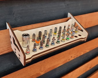 May include: A wooden wall-mounted organizer with a variety of colorful screwdriver bits and a socket wrench. The organizer has a light wood finish and is designed to hold a variety of tools.